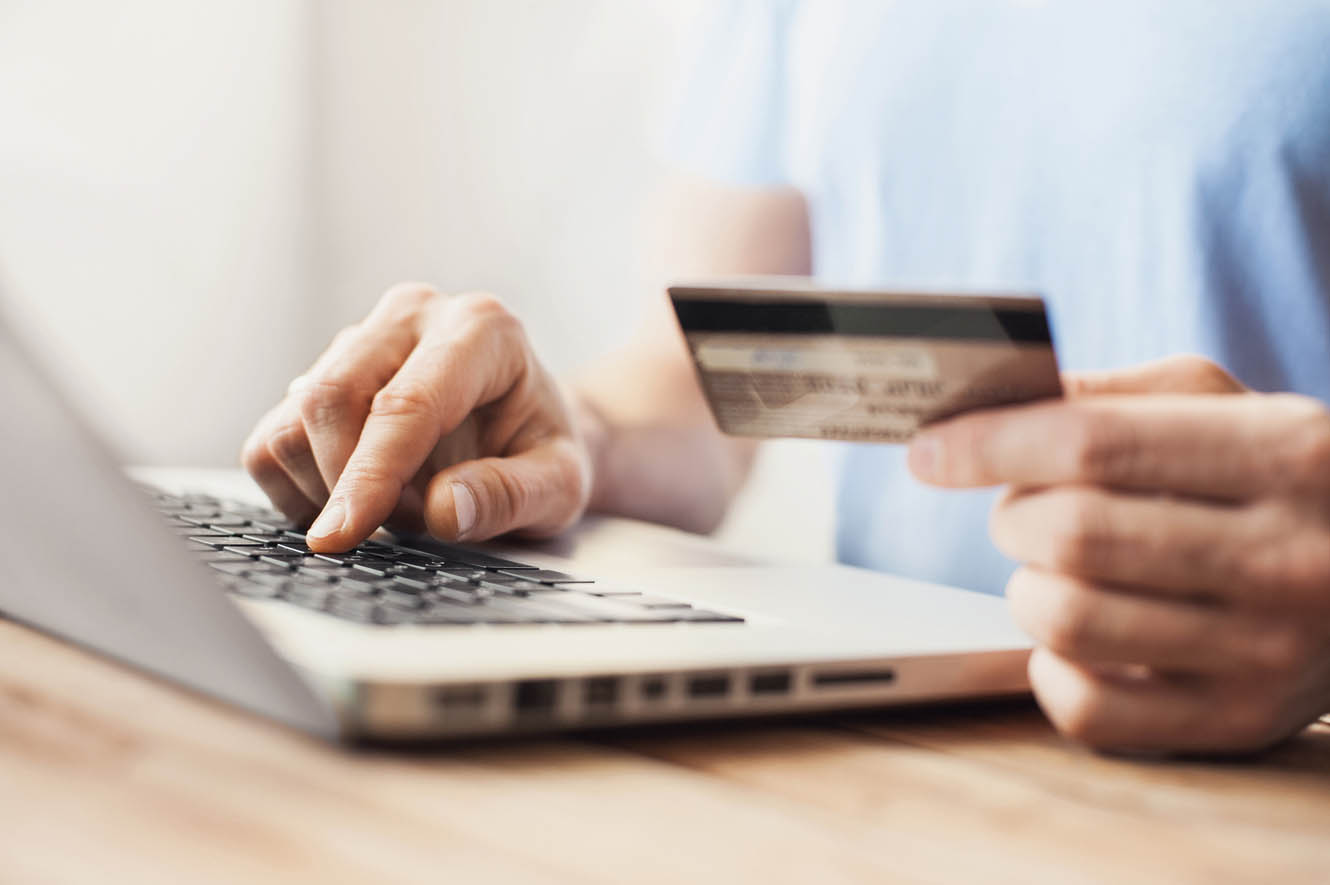 A man types on a keyboard and looks at his credit card.