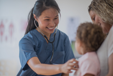 A young nurse uses a stethoscope on a child sitting in her mother's lap.