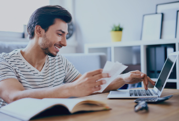 A young man sits at his desk in his home-office and works on his laptop.