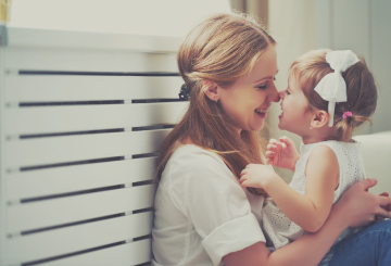 A mother gives her baby a kiss as they sit on the floor in their home
