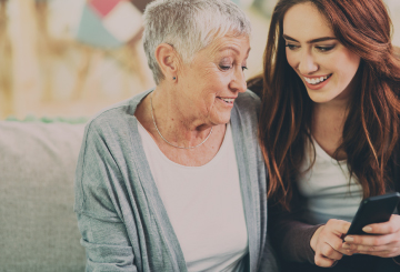 A young woman sits with her grandma and looks at a cellphone.